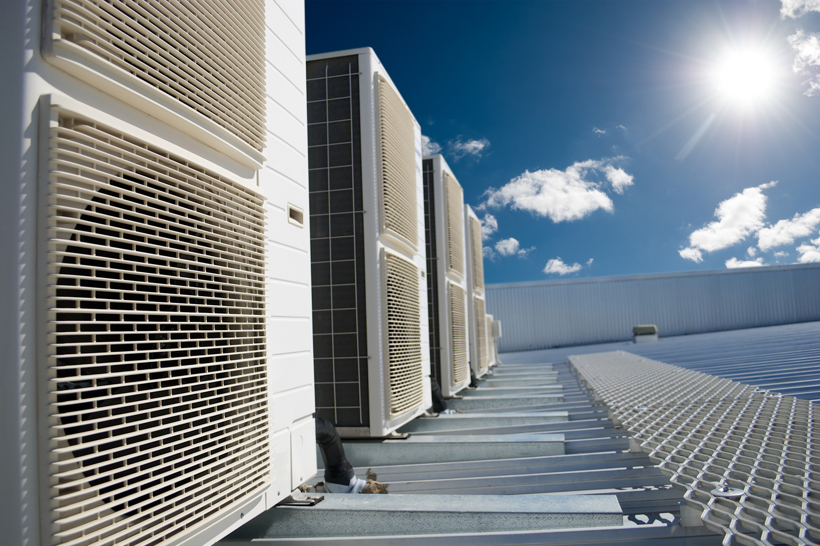 Air conditioner units on a roof of industrial building with blue sky and clouds in the background. Air conditioner units with sun and blue sky